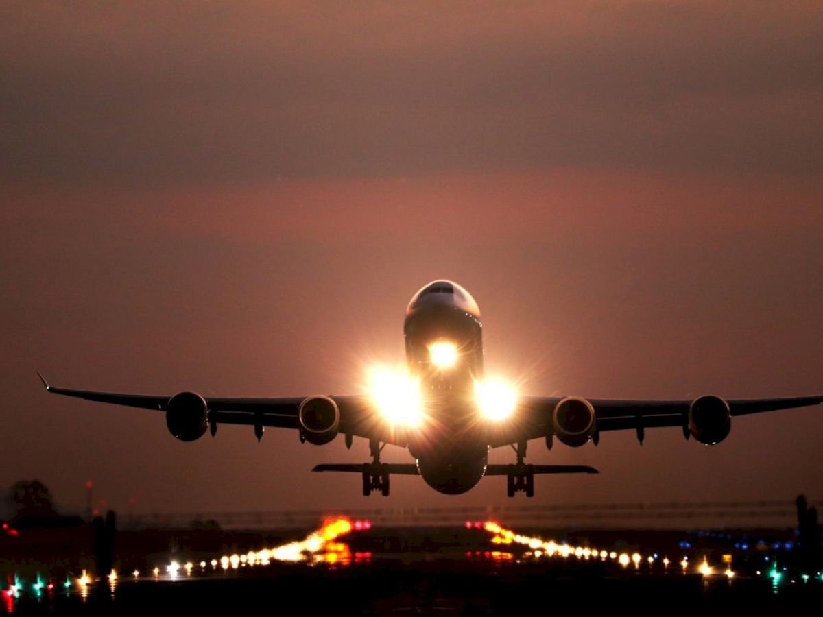 The image shows a large airplane taking off or landing on a runway, with its lights on and the sky appearing to be at dusk or dawn.