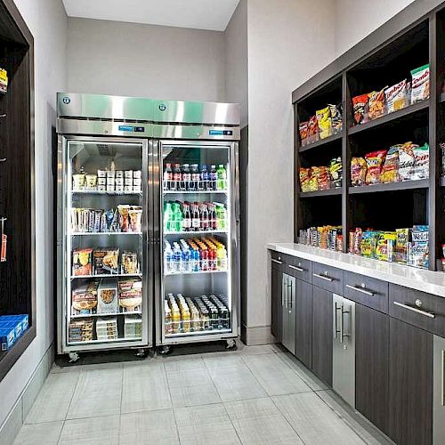 The image shows a well-organized snack room or small convenience store with refrigerated drinks and snacks, plus shelves stocked with various packaged goods.