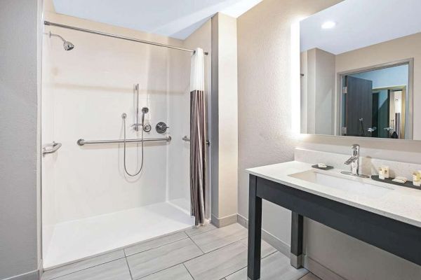 A modern bathroom features a spacious walk-in shower with a curtain, grab bars, and a large vanity with a sink and mirror on the right.